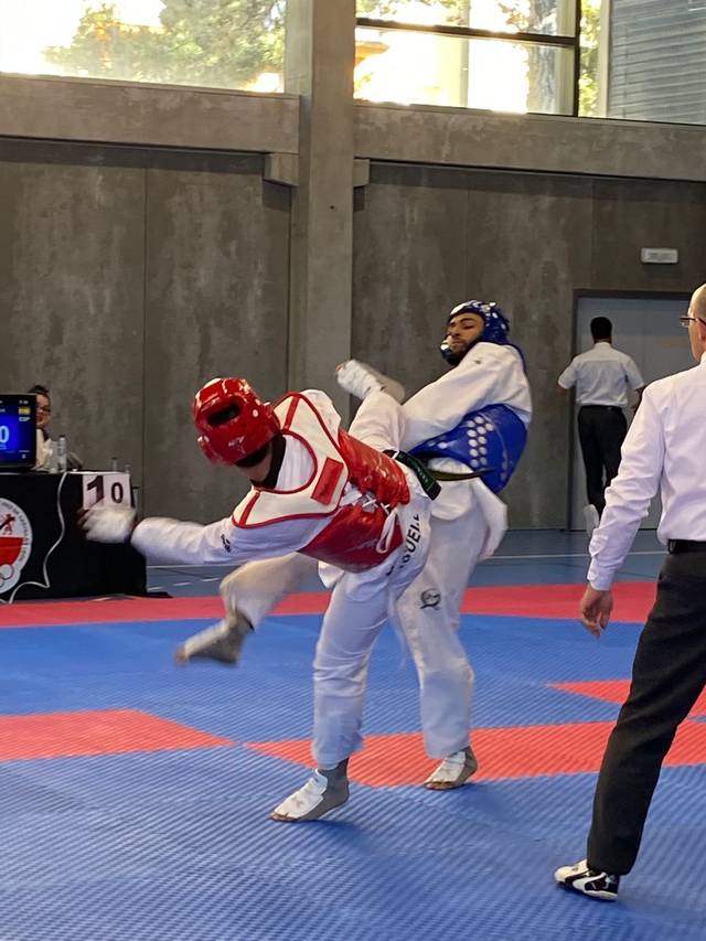 Two taekwondo athletes competing in a match, with one in red and the other in blue protective gear