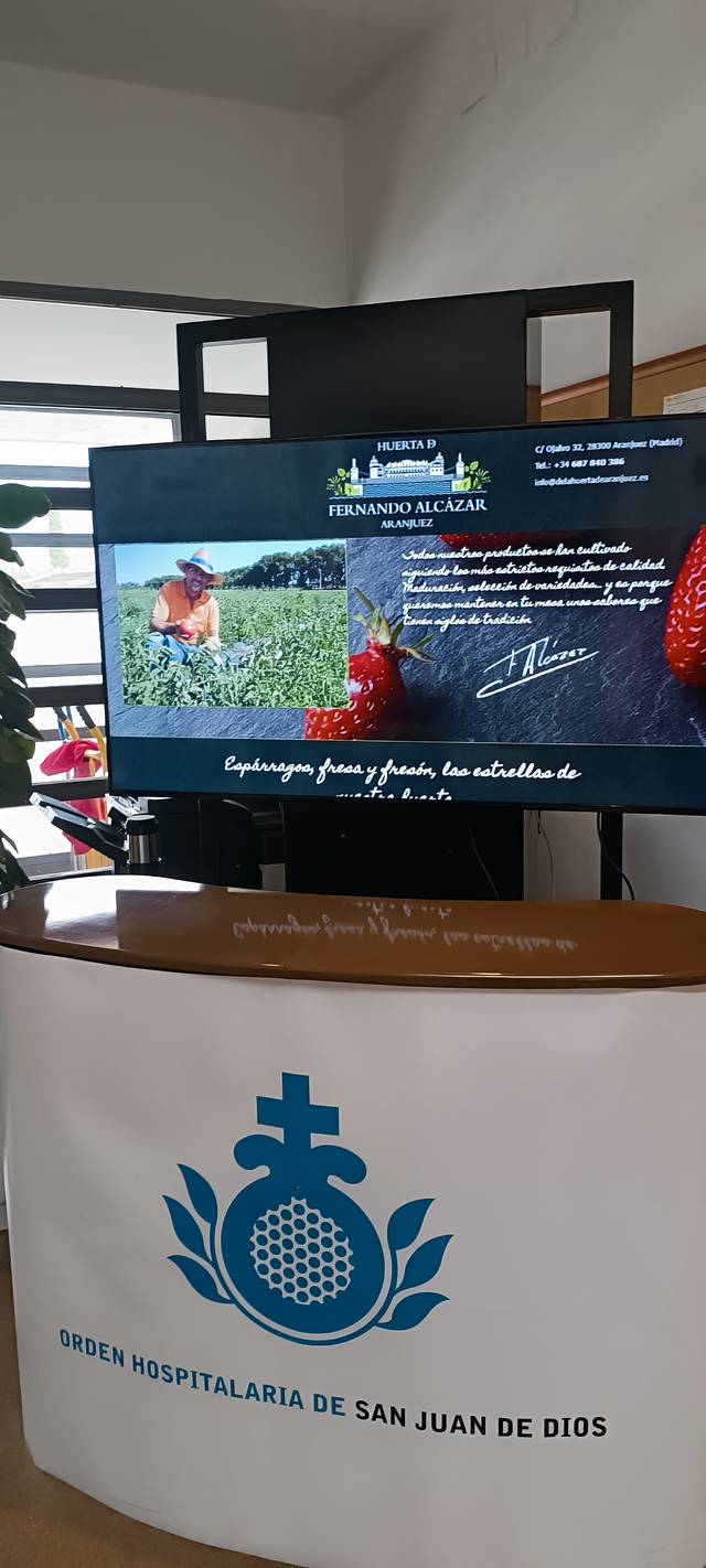 A reception desk displaying a screen with information about Fernando Alcázar and the Hospital Order of San Juan de Dios.