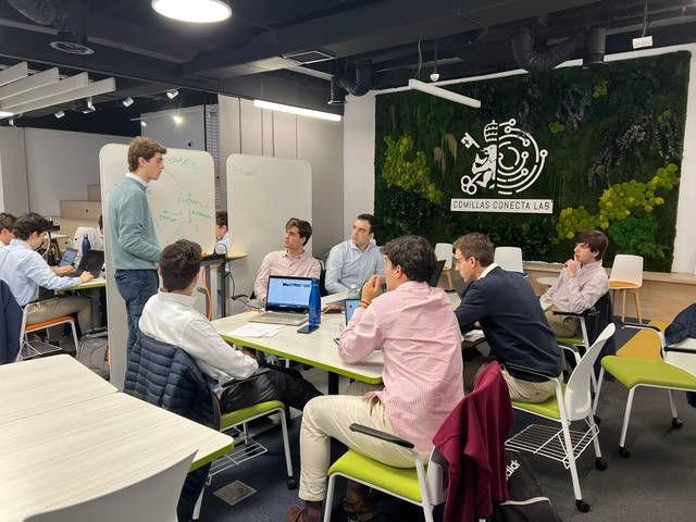 A group of men engaging in a discussion in a modern office setting with laptops and whiteboards.