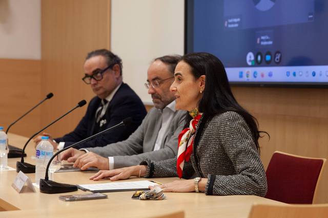 Una mujer habla en una mesa de conferencia, acompañada de dos hombres.