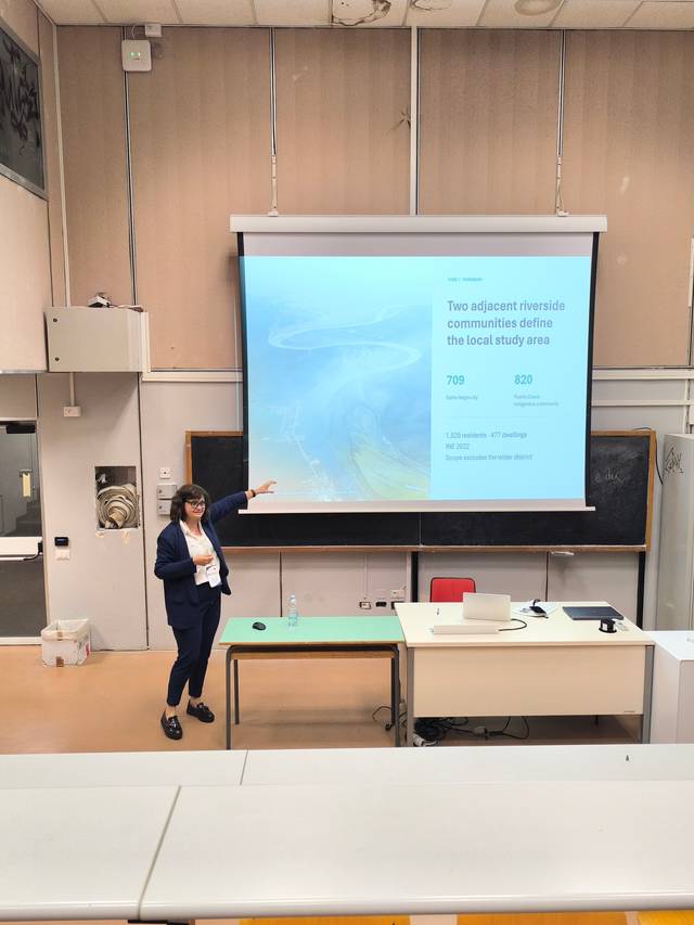 Una presentadora señala una diapositiva durante una conferencia en un aula.