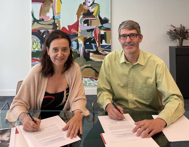 Dos personas están sentadas en una mesa firmando documentos.