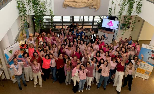 Un gran grupo de personas reunidas en un espacio, vestidas de rosa y levantando las manos en señal de celebración.