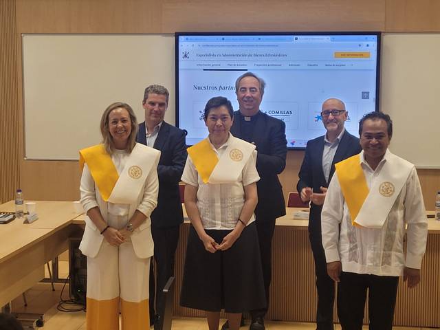 A group of six people, three men and three women, wearing academic robes and sashes, standing in a conference room with a presentation screen in the background.