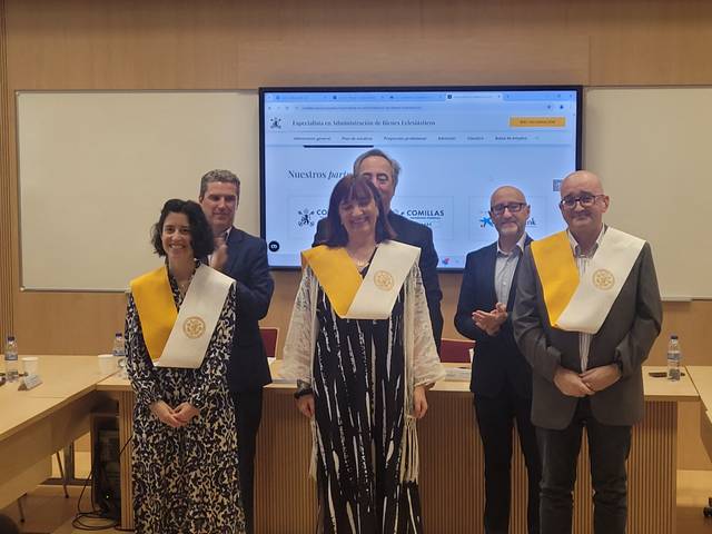 Five people wearing academic robes standing in front of a presentation screen at a university event.