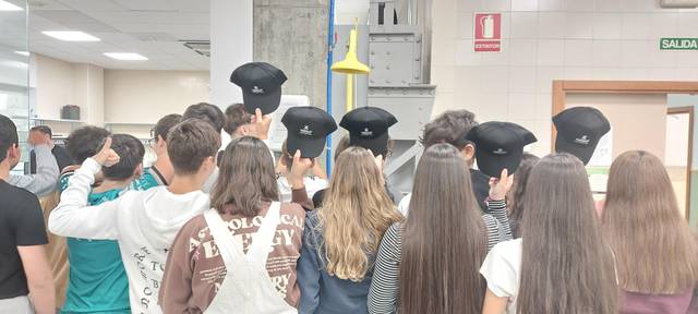 Un grupo de estudiantes en un aula observa atentamente una demostración mientras dos oficiales de policía los supervisan.