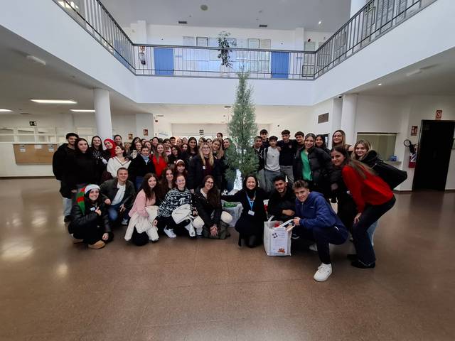 Un grupo de estudiantes posando juntos en un vestíbulo con un árbol de Navidad.