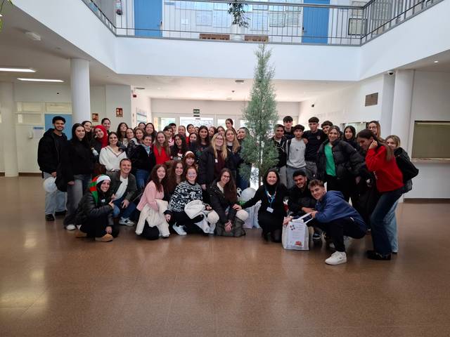 Un grupo de estudiantes posando juntos en un espacio amplio, decorado con un árbol navideño.