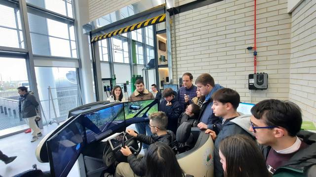 Un grupo de personas observa a un individuo que está conduciendo un simulador de vehículo en un ambiente moderno.