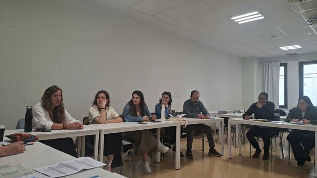 Un grupo de personas sentadas alrededor de una mesa en un aula, participando en una conversación.