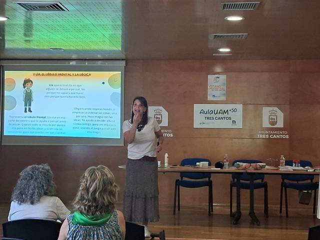 Una presentadora habla frente a un público mientras muestra una diapositiva en una reunión.