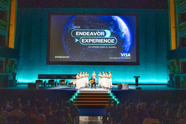 Un evento llamado Endeavor Experience se lleva a cabo en un escenario iluminado con una proyección de un globo terráqueo.