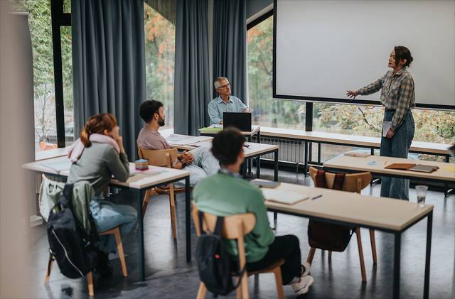 Una mujer da una presentación a un grupo de estudiantes en un aula luminosa.