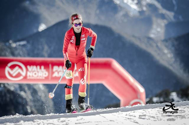 Esquiador en acción en una pista cubierta de nieve con vestimenta roja y gafas, rodeado de montañas.