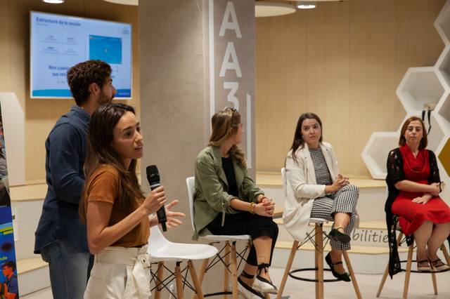 Un grupo de personas discutiendo en un evento mientras una mujer habla con un micrófono.