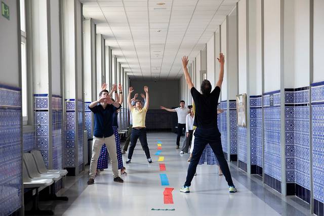 A group of people are joyfully participating in a game involving throwing paper planes in a brightly lit hallway.