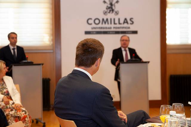 A man in a suit listening intently to a speaker at a formal event hosted by Comillas University.