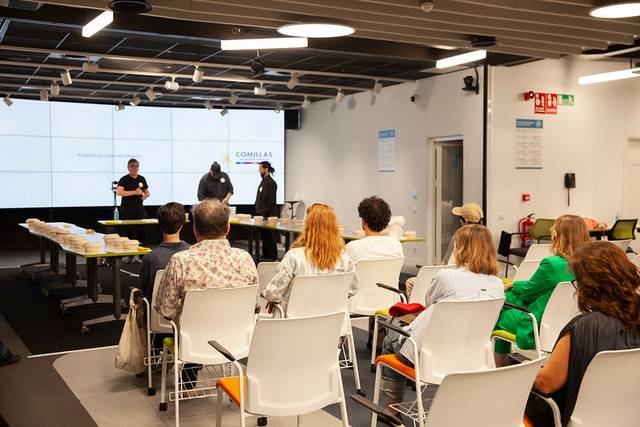 People sitting in a modern classroom with three speakers presenting at the front.