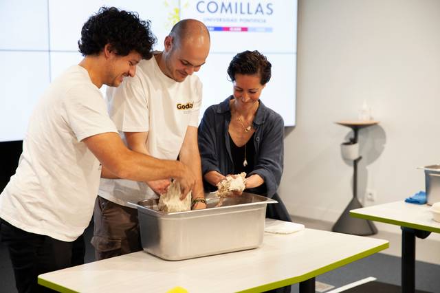 Three people, two men and a woman, are engaging in a cooking class, collaborating while preparing dough in a metal tray.