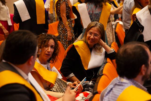 Group of people in academic regalia sitting and chatting at a graduation ceremony.