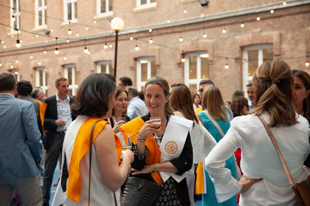 A group of people conversing at an outdoor event, with one woman prominently displaying a medal.