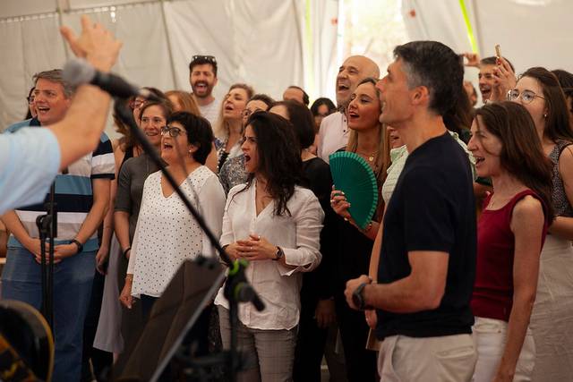 A group of people of various ages enjoying a performance or presentation under a white tent.