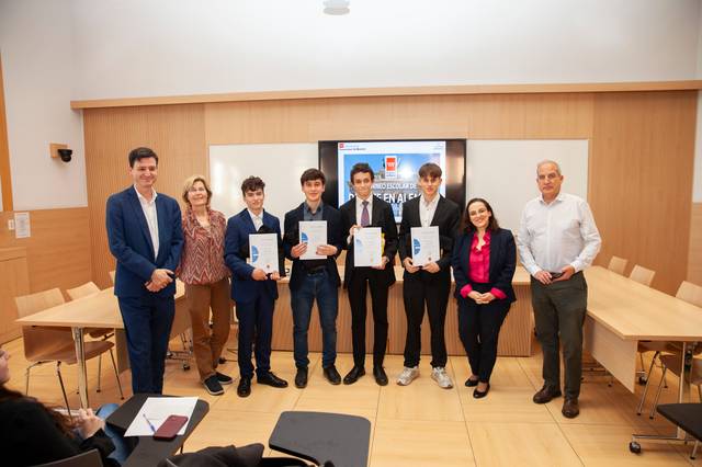 A group of people, including teenagers and adults, are standing in a classroom holding certificates.