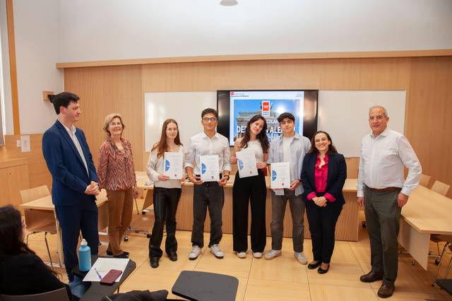Group of people standing in a classroom with certificates, with a presentation screen in the background.