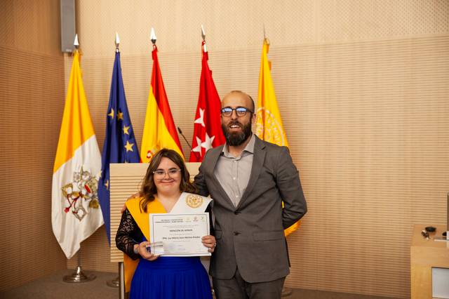 A man and a woman posing with a certificate in a room with multiple flags in the background.