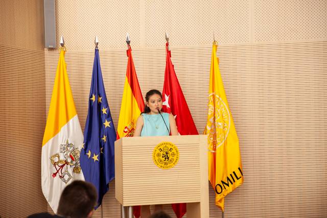 A young girl delivers a speech at a podium with various flags, including the European Union flag, in the background.