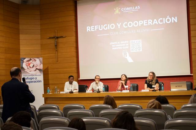 A panel discussion event in a lecture hall with an audience and four speakers discussing 'Refuge and Cooperation'.