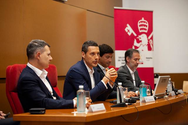 A man speaks at a podium during a panel discussion in a conference room.