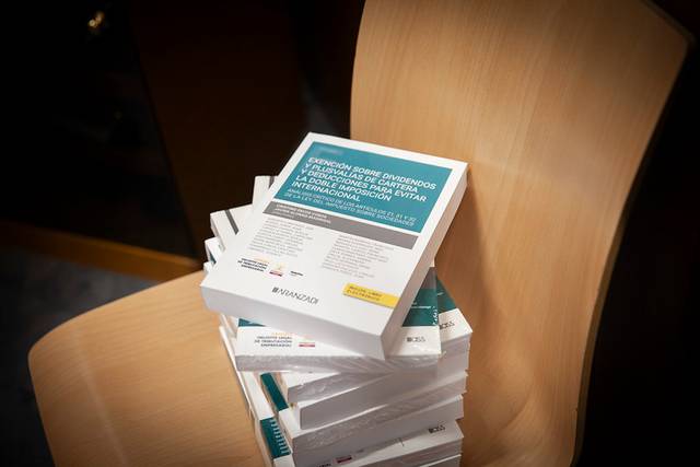 A stack of printed books or reports on a wooden chair in a dimly lit room.