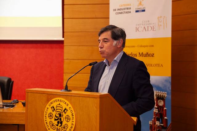 A man is speaking at a podium with a university emblem and banners in the background.