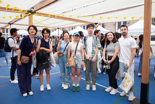 A group of seven people smiling at an outdoor event with yellow festoons and a blue-covered ground.