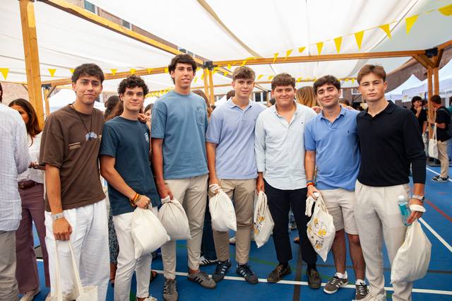 A group of seven young men standing together under a tent at an outdoor event, each holding a tote bag.