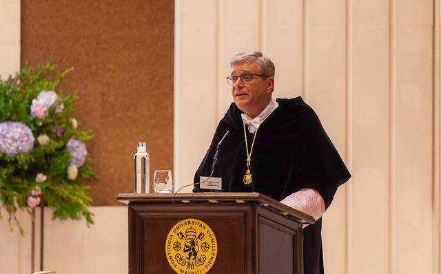 A man in academic regalia speaking at a lectern with a university seal