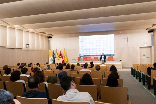 A professional presentation in a modern conference hall with an audience listening to the speaker.