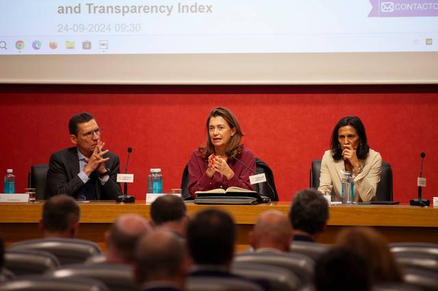 Three professionals are seated at a panel during a conference, engaging with an audience.