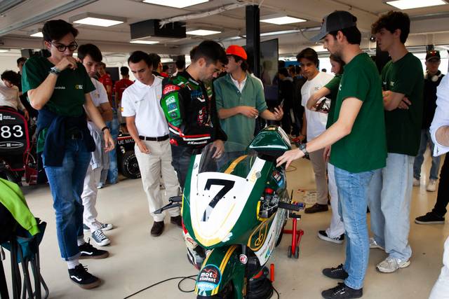 A group of people observing and working on a racing motorcycle in a garage.