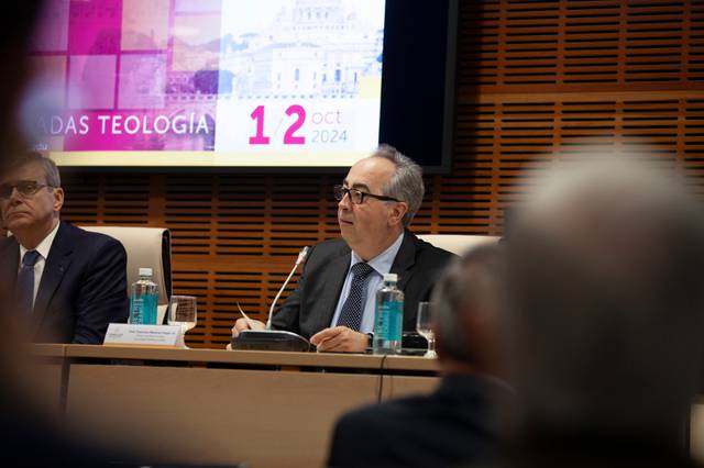 A man speaking at a podium during a panel discussion, with a date '12 Oct 2024' visible on a digital display in the background.