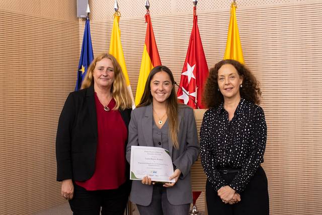 Three women posing for a photo at an award ceremony, with one holding a certificate.