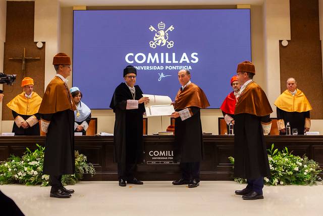 A formal academic event at Comillas Pontifical University where a person is receiving a certificate.