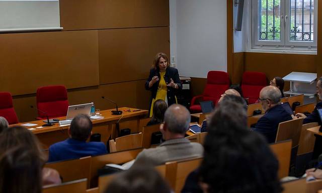 A woman is presenting in front of an audience in a lecture hall.