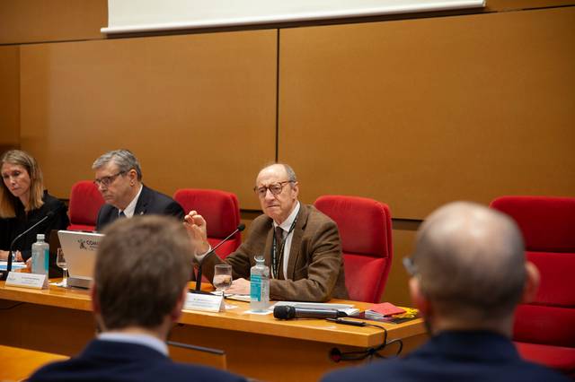 A man is speaking at a conference table while others listen in a meeting room.