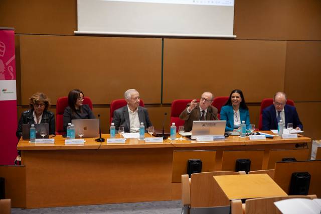 A group of six professionals, including three women and three men, sit at a panel in a conference room, engaging with the audience.