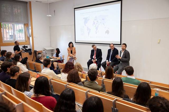 A group of professionals conducting a presentation in a lecture hall filled with attendees.