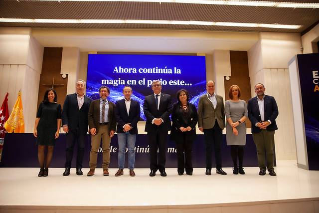 A group of people standing on a stage during a presentation with a large projected text behind them.