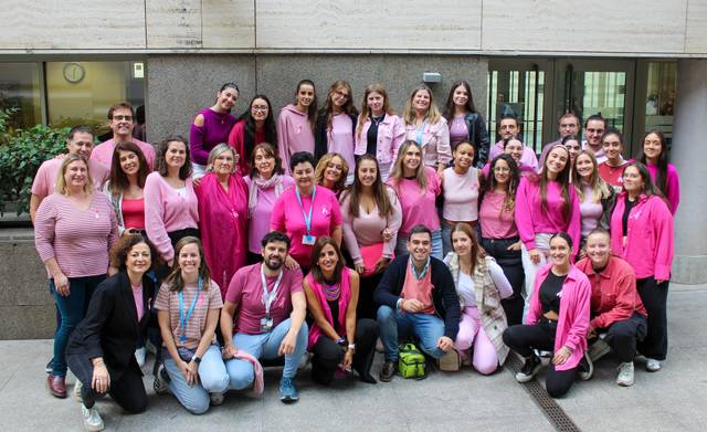 A large group of people wearing pink shirts posing together in an outdoor setting.