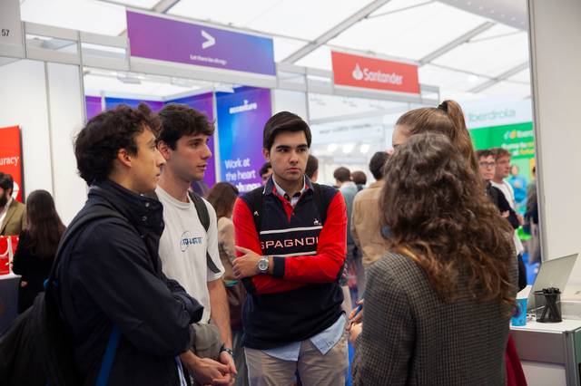 A group of students is engaging in a conversation with a representative at a career fair booth.